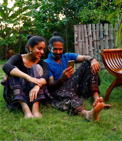 A happy couple sitting on a green lawn and viewing mobile 